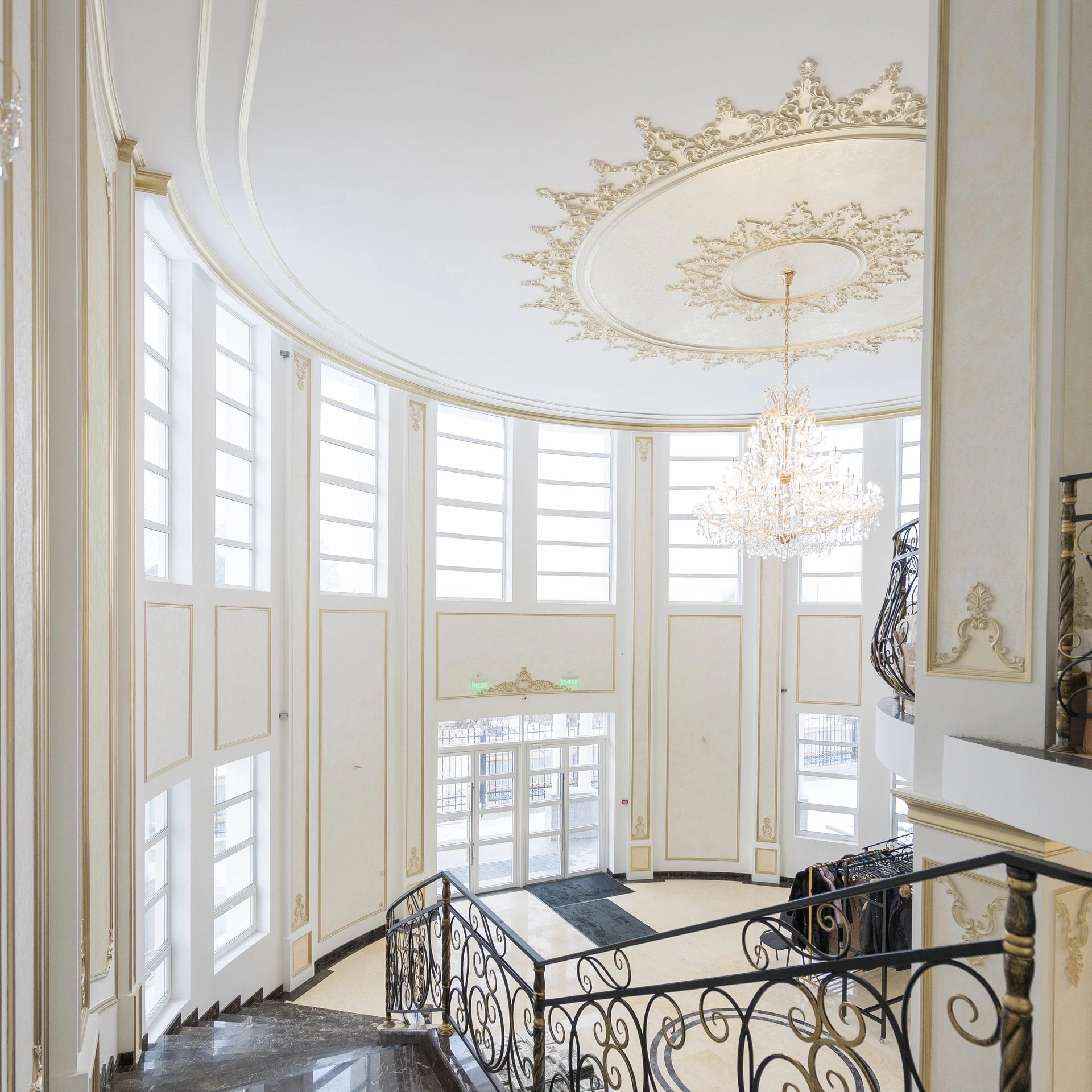 Double-height entrance hall with a chandelier, gold-toned moldings and stairs with decorative metal railings