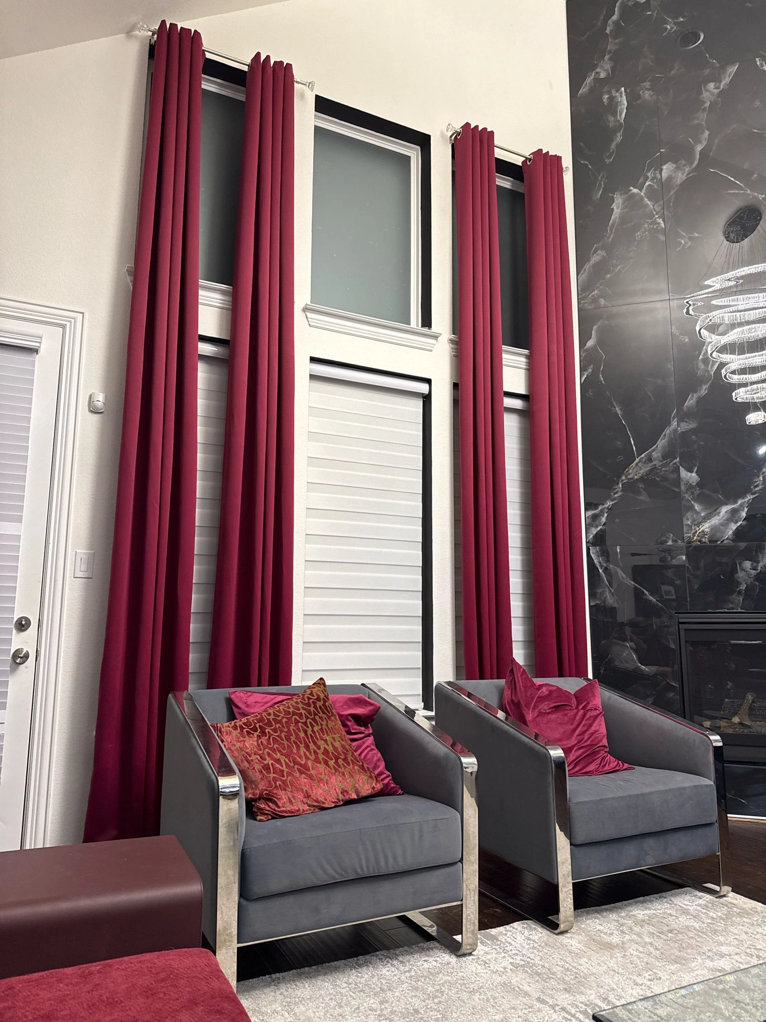 Living room with tall burgundy curtains, gray armchairs and a dark veined wall beside a fireplace
