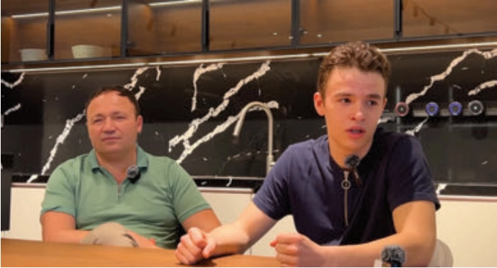 Two men seated at a table in front of a black veined kitchen backsplash