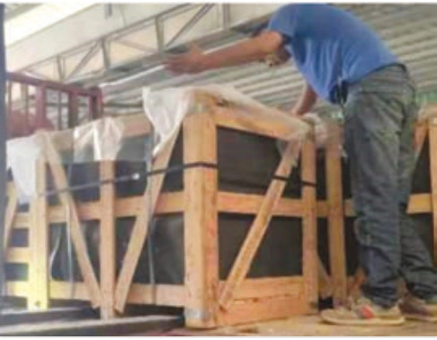 Worker leaning over a wooden shipping crate containing wrapped panels