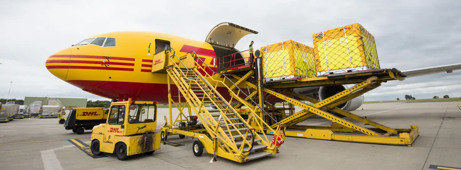 Netted cargo pallets on a raised loading platform beside a yellow DHL aircraft