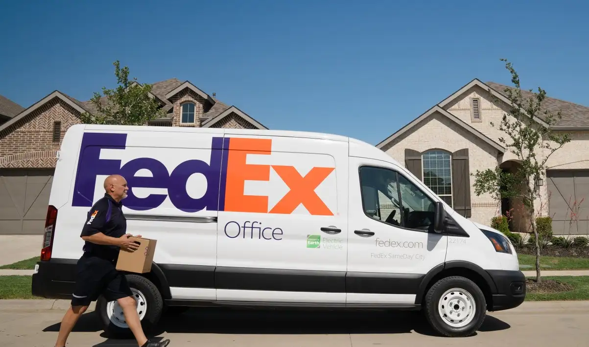 Courier carrying a cardboard parcel beside a white FedEx delivery van on a residential street