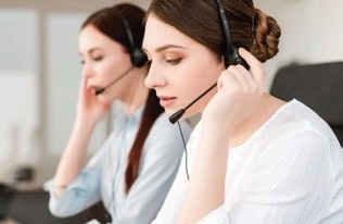 Two customer support agents wearing headsets with microphones at desks