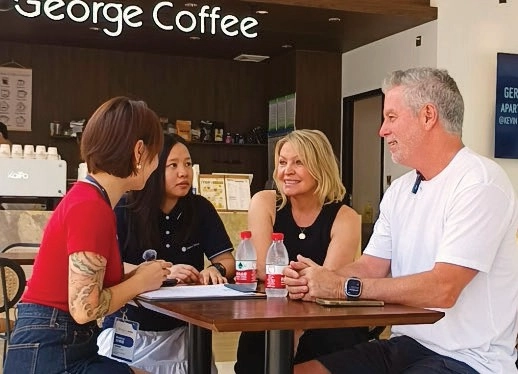 Four people talking around a table with water bottles and papers beneath a George Coffee sign