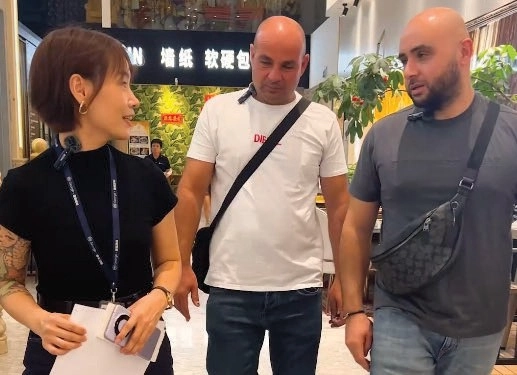 Three people talking in a showroom, with the woman holding papers and wearing a lanyard