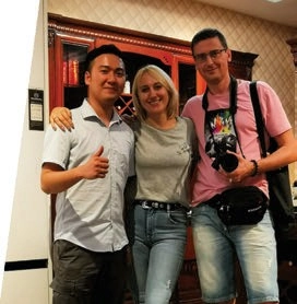 Three people posing in front of a wooden display cabinet, one holding a camera