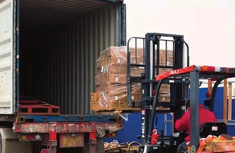 Red forklift lifting a wrapped pallet beside the open doors of a shipping container