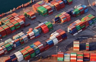 Aerial view of rows of multicolored shipping containers in a terminal beside the water